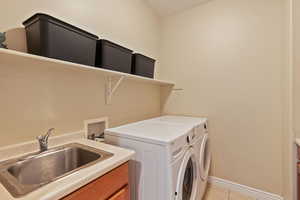 Clothes washing area featuring independent washer and dryer, cabinet space, a sink, light tile patterned floors, and baseboards