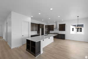 Kitchen with wall chimney range hood, decorative backsplash, light wood-type flooring, stainless steel microwave, and an island with sink