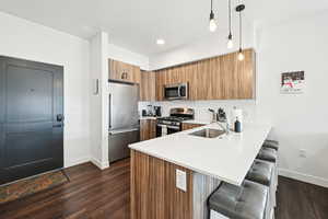 Kitchen featuring appliances with stainless steel finishes, a sink, a breakfast bar area, brown cabinetry, and a peninsula