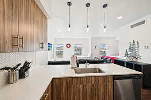 Kitchen featuring a sink, dishwasher, light countertops, decorative backsplash, and visible vents