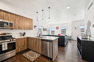 Kitchen with stainless steel appliances, a textured ceiling, and brown cabinetry
