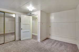 Unfurnished bedroom with carpet floors, visible vents, a wainscoted wall, and a closet
