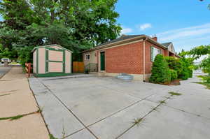View of property exterior with a chimney, an outbuilding, brick siding, fence, and a shed