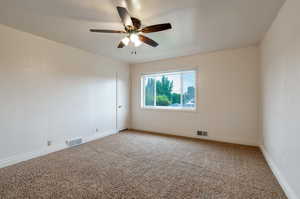 Empty room with a ceiling fan, light colored carpet, and visible vents