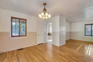 Empty room with a chandelier, baseboards, visible vents, and light wood finished floors