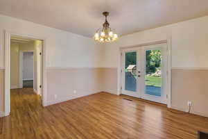 Empty room with a chandelier, french doors, visible vents, and wood finished floors