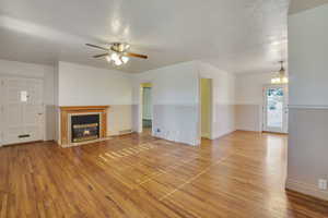 Unfurnished living room with visible vents, light wood-style floors, baseboards, a fireplace with flush hearth, and ceiling fan with notable chandelier