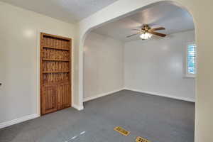 Spare room with a ceiling fan, a textured ceiling, arched walkways, baseboards, and dark carpet