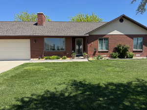Ranch-style house featuring driveway, a chimney, a front yard, a garage, and brick siding