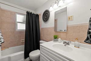 Full bath with vanity, wainscoting, shower / bath combination with curtain, toilet, and tile walls