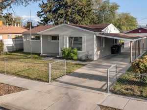 View of front of property with a carport, a fenced front yard, concrete driveway, and a front lawn