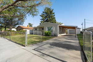 View of front of property with fence private yard, driveway, a front yard, an outbuilding, and a carport
