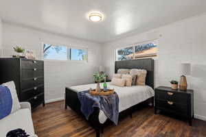 Bedroom #1 featuring baseboards, dark wood-style flooring, and brick wall