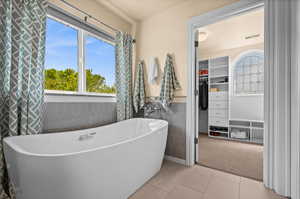 Full bathroom with tile patterned flooring, wainscoting, tile walls, a spacious closet, and a free standing tub
