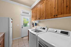 Washroom with crown molding, cabinet space, baseboards, light tile patterned flooring, and washer and dryer