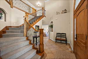 Entrance foyer with crown molding, stairs, baseboards, light tile patterned floors, and a towering ceiling