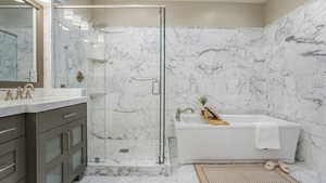 Bathroom featuring a soaking tub, tile walls, a marble finish shower, and vanity