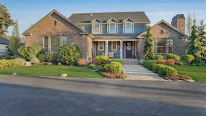 View of front facade with covered porch, a chimney, a front yard, and brick siding