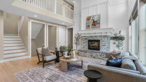 Living area with wood-type flooring, stairs, a towering ceiling, a stone fireplace, and recessed lighting