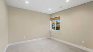 Empty room featuring light colored carpet, recessed lighting, and visible vents