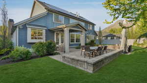 Back of property with roof mounted solar panels, fence, a lawn, and a patio area