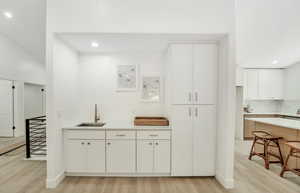 Kitchen with a sink, light wood finished floors, light countertops, recessed lighting, and white cabinetry