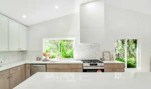 Kitchen with light stone counters, appliances with stainless steel finishes, a sink, lofted ceiling, and tasteful backsplash