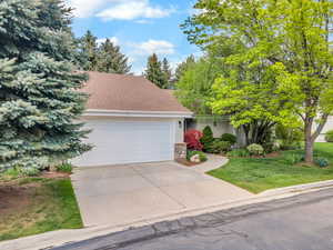View of front of house featuring an attached garage, a shingled roof, a front lawn, stone siding, and concrete driveway