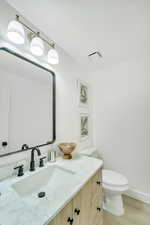 Half bathroom featuring vanity, toilet, baseboards, wood finished floors, and visible vents