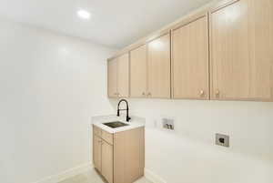 Laundry room featuring electric dryer hookup, cabinet space, a sink, baseboards, and hookup for a washing machine