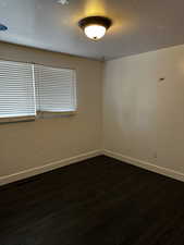 Empty room featuring dark wood-type flooring, baseboards, and visible vents