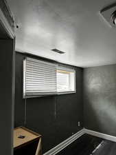 Spare room featuring visible vents, a textured wall, wood finished floors, baseboards, and a textured ceiling
