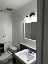 Bathroom with toilet, a textured wall, visible vents, and a sink