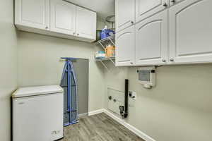 Clothes washing area featuring light wood-type flooring, cabinet space, baseboards, and hookup for an electric dryer