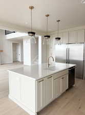 Kitchen featuring high end refrigerator, a sink, an island with sink, light wood-type flooring, and light stone countertops