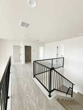 Corridor with a textured ceiling, visible vents, light colored carpet, and an upstairs landing