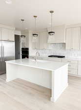Kitchen featuring light countertops, a sink, gas cooktop, built in refrigerator, and decorative backsplash