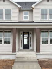 View of exterior entry with a porch and a shingled roof