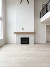 Unfurnished living room with a tile fireplace, wood finished floors, and a towering ceiling
