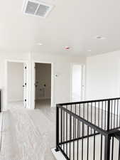 Hallway featuring a textured ceiling, baseboards, visible vents, an upstairs landing, and light colored carpet
