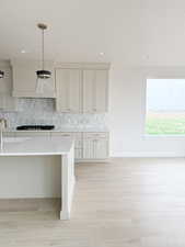 Kitchen with decorative backsplash, light wood-style floors, premium range hood, pendant lighting, and black stovetop