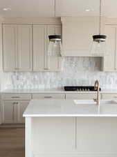 Kitchen featuring a textured ceiling, decorative backsplash, wood finished floors, light stone countertops, and hanging light fixtures