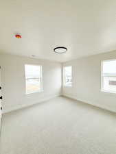 Unfurnished room featuring visible vents, baseboards, a textured ceiling, and light colored carpet