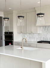Kitchen featuring stainless steel gas stovetop, a sink, backsplash, and double oven