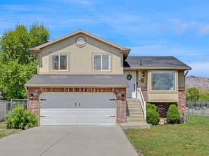 Split level home featuring brick siding, fence, a front lawn, concrete driveway, and an attached garage