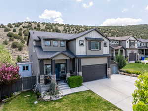 View of front of home with a front yard, a garage, fence, concrete driveway, and stone siding