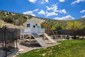 View of playground with a fenced backyard, a lawn, a trampoline, an outdoor fire pit, and a forest view