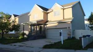 View of front of home with stucco siding, fence, stone siding, and a garage