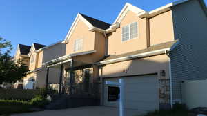 Back of property featuring fence, stone siding, a garage, stucco siding, and covered porch