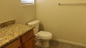 Bathroom with toilet, baseboards, wood finished floors, and vanity